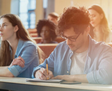 Hispanic Young Man Among His Fellow Students in the Classroom. Young Bright People Listening to a Lecture and Take Notes while Studying at the University.